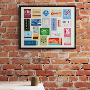 May include: A framed collage of matchbox labels from various restaurants and bars. The labels feature colorful designs and text, including names like "Clocked!", "South Kitchen + Bar", "Pauley's", and "Seabear".
