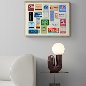 May include: A framed collage of vintage matchbox labels featuring various restaurant and bar names, including "Ted's", "Place", "Porpoise House Grill", "Clocked", "National", "Seabear", "Lesr Roast Grill", "Paloma", "Pauley's", "Creature Comfort", "South Kitchen + Bar", and "Chuck's Fish".