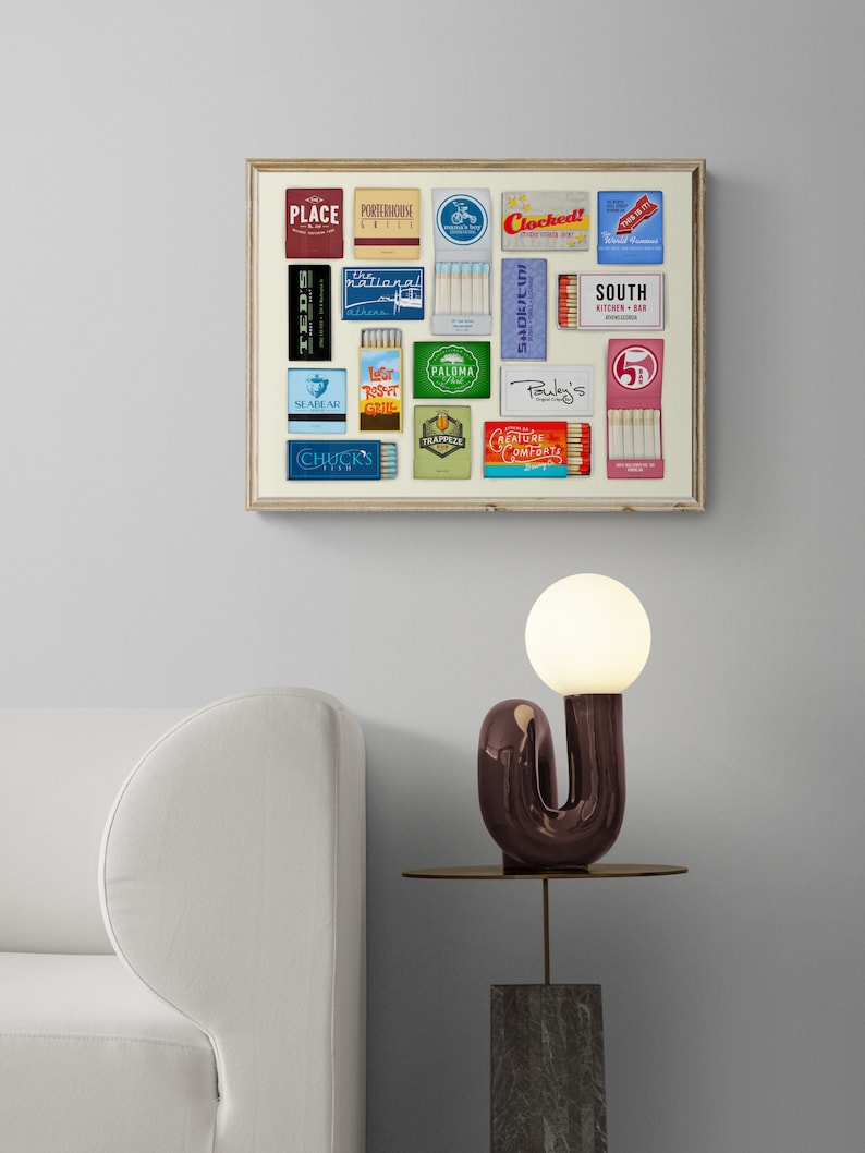 May include: A framed collage of vintage matchbox labels featuring various restaurant and bar names, including "Ted's", "Place", "Porpoise House Grill", "Clocked", "National", "Seabear", "Lesr Roast Grill", "Paloma", "Pauley's", "Creature Comfort", "South Kitchen + Bar", and "Chuck's Fish".