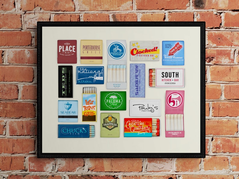May include: A framed collage of matchbox labels featuring various restaurants and businesses. The labels are in a variety of colors and designs, including red, blue, green, and yellow. Some of the labels feature text, such as "The National", "Seabear", "Clocked!", and "South Kitchen + Bar".