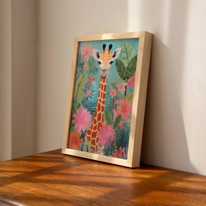 Op de afbeelding: Een ingelijste illustratie van een giraffe met een lichtbruin en oranje patroon op zijn vacht, die in een veld met roze en oranje bloemen staat. De achtergrond is lichtblauw.