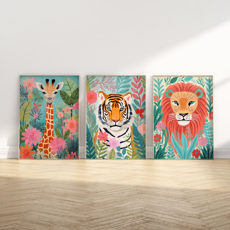 Op de afbeelding: Drie ingelijste prints met kleurrijke illustraties van een giraffe, een tijger en een leeuw. Elke print toont een junglesc&egrave;ne met weelderig groen gebladerte en levendige roze bloemen.
