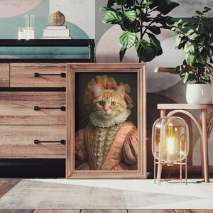 K&ouml;nnte beinhalten: Ein gerahmtes Portr&auml;t einer rotbraunen Katze, die ein rosa-wei&szlig;es Kleid und ein wei&szlig;es Spitzenkragen tr&auml;gt. Das Portr&auml;t h&auml;ngt an einer Wand in einem Raum mit einer Kommode aus Holz und einem Stuhl.