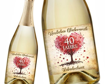 May include: Two bottles of sparkling wine with labels that say "Herzlichen Glückwunsch 40 Jahre Rubinhochzeit". The labels feature a red heart-shaped tree with the number 40 in the center.