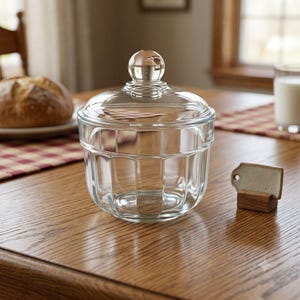 May include: A clear glass jar with a matching lid featuring a spherical knob handle. The jar has a rounded base with vertical fluted panels around the exterior. The glass is transparent, allowing a clear view through the container walls.