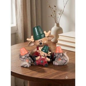 May include: A set of three ceramic animal figurines featuring a large deer wearing a green pot hat and red overalls, flanked by two smaller squirrel-like creatures wearing orange pot hats, all with painted facial features and textured details.