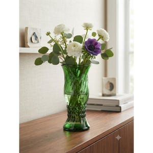 Peut inclure: Un grand vase en verre vert émeraude doté d'une texture torsadée et en spirale sur tout son corps. Le vase contient un bouquet de renoncules blanches, de feuilles d'eucalyptus vertes et une unique fleur d'anémone violette éclatante.