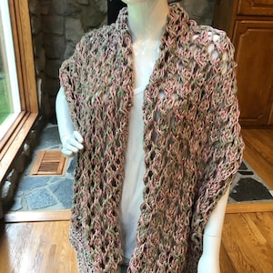 May include: A sleeveless open-front cardigan featuring a loose, chunky crochet knit pattern. The yarn is a variegated blend of soft pink, sage green, and cream tones. The garment has a textured, airy construction with a ribbed hem along the bottom edge.