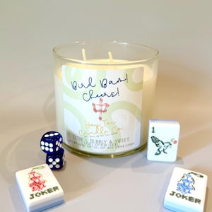 May include: A three-wick soy wax candle in a clear glass jar with a label reading Bird Bam! Cheers! Hop Tai Candle Co. Citrus, Bubbly & Sweet. Net wt. 14 oz. (397 g). Two blue dice and two white mahjong tiles with joker and bird graphics are nearby.