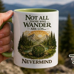 May include: A white ceramic mug with a light green interior and handle. The mug features a graphic of a twenty-sided die in a forest landscape with mountains and the text: Not all those who wander are los... Nevermind.