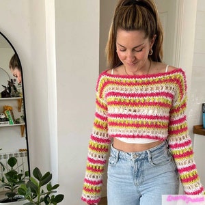 May include: A pink, white, and yellow striped crochet sweater with long sleeves. The sweater is cropped and has a loose fit.