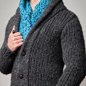 May include: A dark gray knitted cardigan with a shawl collar and two buttons. The cardigan is worn over a blue and green patterned scarf.