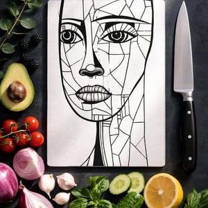 May include: A white cutting board with a black and white geometric face design, surrounded by fresh produce and a knife. The produce includes tomatoes, avocado, red onion, garlic, basil, cucumber, lemon, and blackberries.