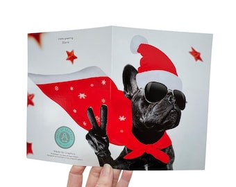 Könnte beinhalten: Eine Weihnachtskarte mit einem schwarzen Französischen Bulldoggen, der einen Weihnachtsmann-Hut und eine Sonnenbrille trägt und ein Peace-Zeichen zeigt. Der Hund trägt einen roten Umhang und ein rotes Bandana. Die Karte hat einen weißen Hintergrund mit roten Sternen und Schneeflocken.