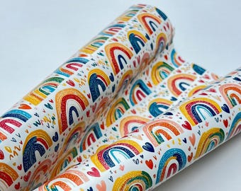 May include: Rolls of white paper with a colorful rainbow pattern. The design features rainbows in red, orange, yellow, blue, and green, along with hearts and small yellow accents. The paper is likely used for wrapping gifts or crafting.