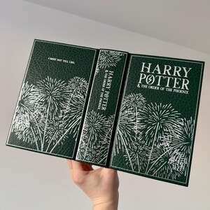 May include: A green hardcover book with a silver embossed design of fireworks. The book title is "Harry Potter and the Order of the Phoenix".