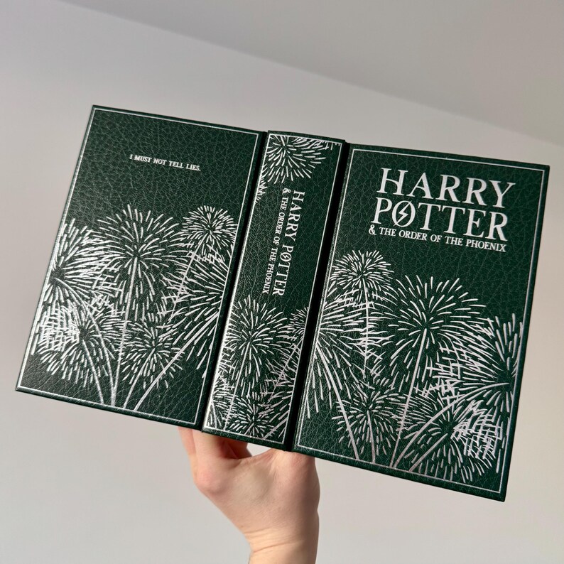 May include: A green hardcover book with a silver embossed design of fireworks. The book title is "Harry Potter and the Order of the Phoenix".