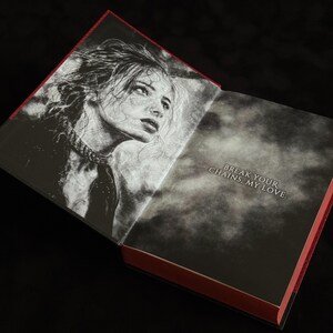 May include: An open hardcover book with red edges. The left page features a black and white sketch of a person with messy hair and a choker. The right page is a dark, smoky background with the white text: BREAK YOUR CHAINS, MY LOVE.