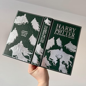 May include: A green hardcover book with a silver embossed design of Dementors from the Harry Potter series. The title "Harry Potter & The Prisoner of Azkaban" is printed in silver on the front cover.