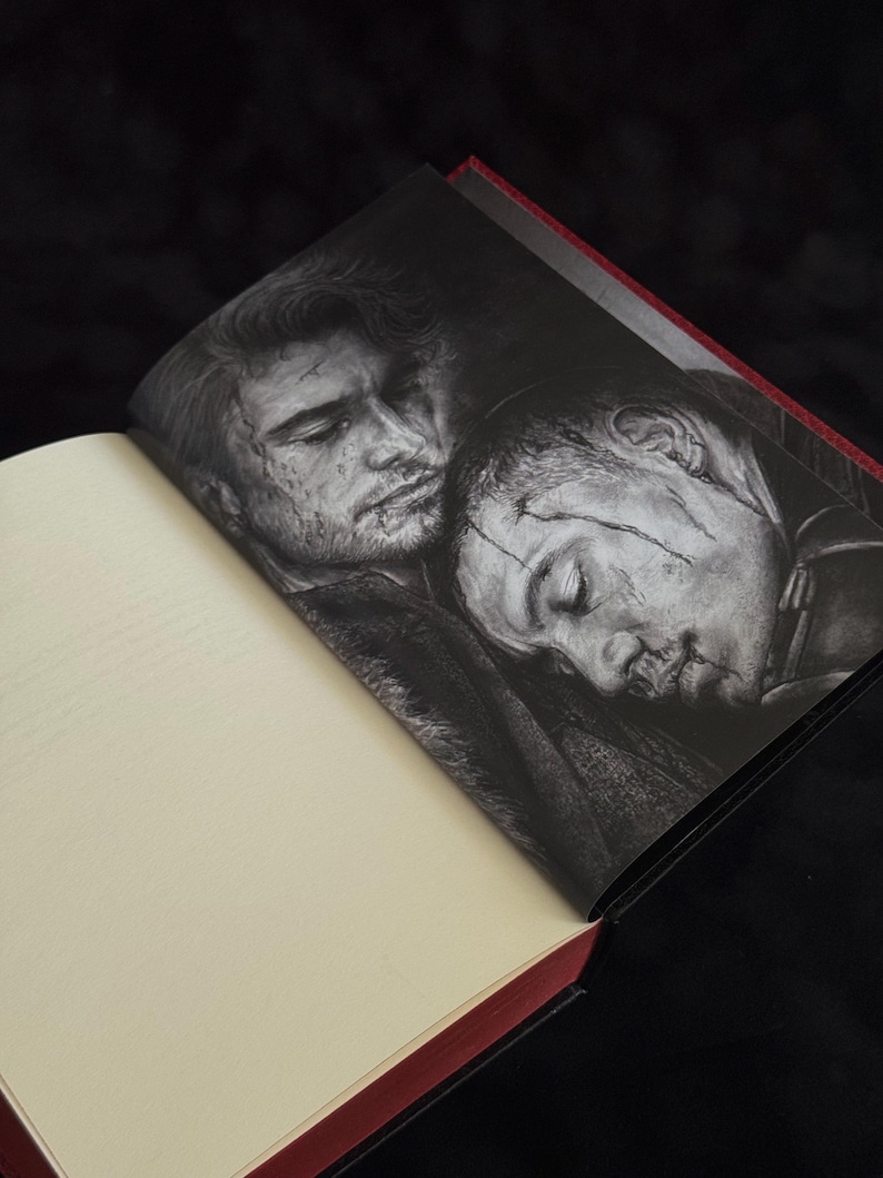 May include: An open hardcover book featuring a black and white illustration on the right page. The artwork depicts two individuals with facial scars resting their heads together. The book has cream-colored pages and a dark red spine edge.