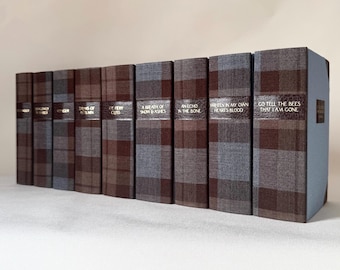 May include: A set of hardcover books with brown, blue, and grey plaid covers. Each book features a brown leather band with gold lettering. Titles include "An Echo in the Bone" and "Written in My Own Heart's Blood."