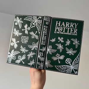 May include: A green hardcover book with a silver embossed design of keys and leaves. The title "Harry Potter & The Philosopher's Stone" is printed in silver on the front cover.
