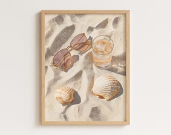 Puede incluir: Una impresión enmarcada que presenta una escena de playa con gafas de sol, un vaso de bebida helada y conchas marinas sobre arena. Las gafas de sol tienen una montura marrón claro. Las conchas son beige y blancas. El vaso está lleno de cubitos de hielo y un líquido claro.