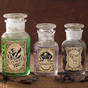 Pu&ograve; includere: Tre bottiglie da farmacia vintage con tappi in vetro. Ogni bottiglia ha un'etichetta con le parole "Gillyweed", "Aconitum" e "Bezoar". Le bottiglie contengono liquidi verdi, viola e grigi. Le etichette hanno bordi decorativi e le parole "Mystic Apothecary".