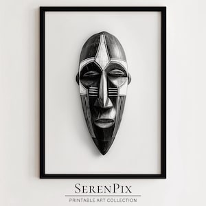 May include: Black and white wooden mask with geometric patterns. The mask has a long, narrow shape with a pointed chin and a flat forehead. The eyes are closed and the mouth is slightly open. The mask is framed in a black frame.
