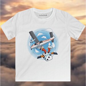 Puede incluir: Camiseta blanca con una ilustración de dibujos animados de un dado con piernas que salta en paracaídas desde un avión. El avión está boca abajo y el dado lleva un mono rojo y blanco. El texto "The Para Dice" está en el avión.