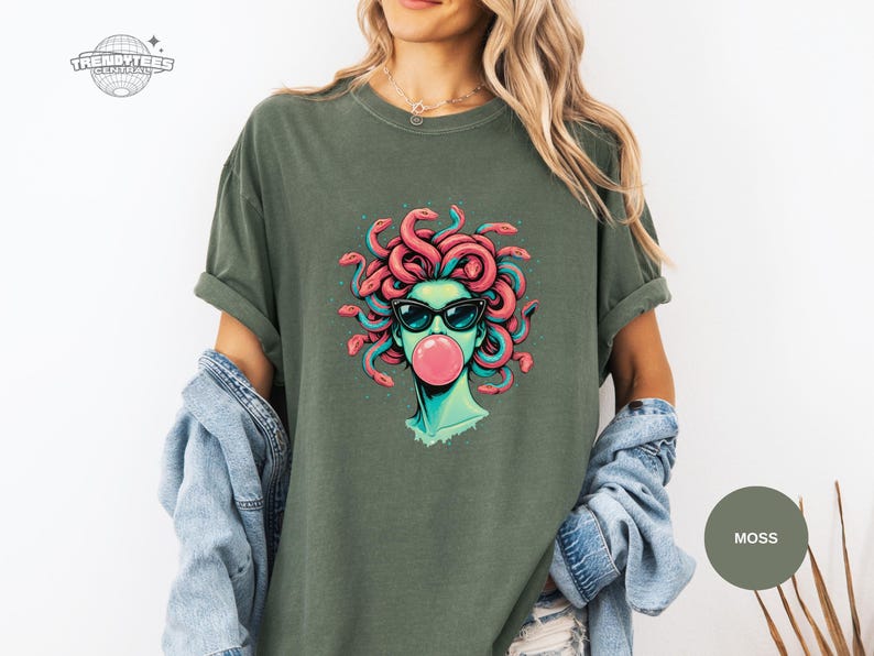 Moss green Comfort Colors tee with the Medusa sunglasses-and-bubblegum design printed front and center. The teal face tones blend well with the muted green shirt for a cool-toned look. Great lifestyle mockup for outdoorsy or casual street style.