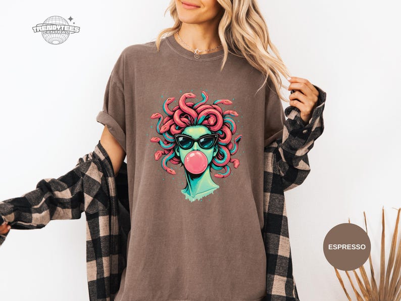 Espresso brown Comfort Colors tee with a centered Medusa portrait wearing black sunglasses and blowing a pink bubblegum bubble. Coral snake hair and teal shading give the graphic a bold pop against the warm neutral tone. Styled for casual winter layering with a flannel vibe.