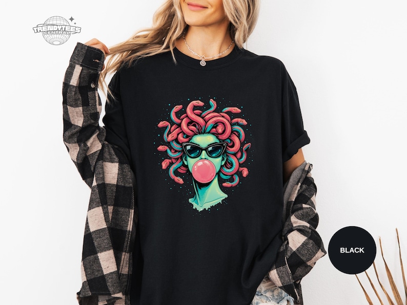 Black Comfort Colors shirt with the Medusa sunglasses portrait and bright pink bubblegum bubble printed at center chest. The coral snake hair and teal face tones create strong contrast on the black fabric. This mockup feels like classic streetwear styling.