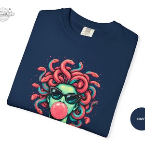 Folded navy Comfort Colors 1717 tee showcasing a close-up of the Medusa bubblegum artwork across the upper chest area. The deep navy makes the coral snake hair and pink bubblegum look vivid and saturated. This image signals fabric quality and print clarity.