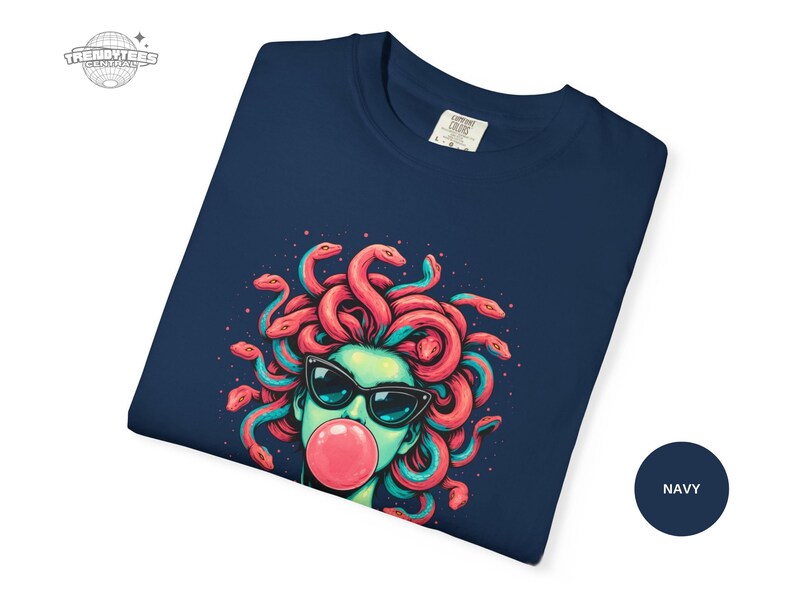 Folded navy Comfort Colors 1717 tee showcasing a close-up of the Medusa bubblegum artwork across the upper chest area. The deep navy makes the coral snake hair and pink bubblegum look vivid and saturated. This image signals fabric quality and print clarity.