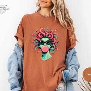 Yam orange-brown Comfort Colors tee with the Medusa bubblegum graphic centered. The warm shirt tone gives the art a retro, desert palette feel while the teal highlights keep it modern. Styled for an earthy, casual wardrobe.