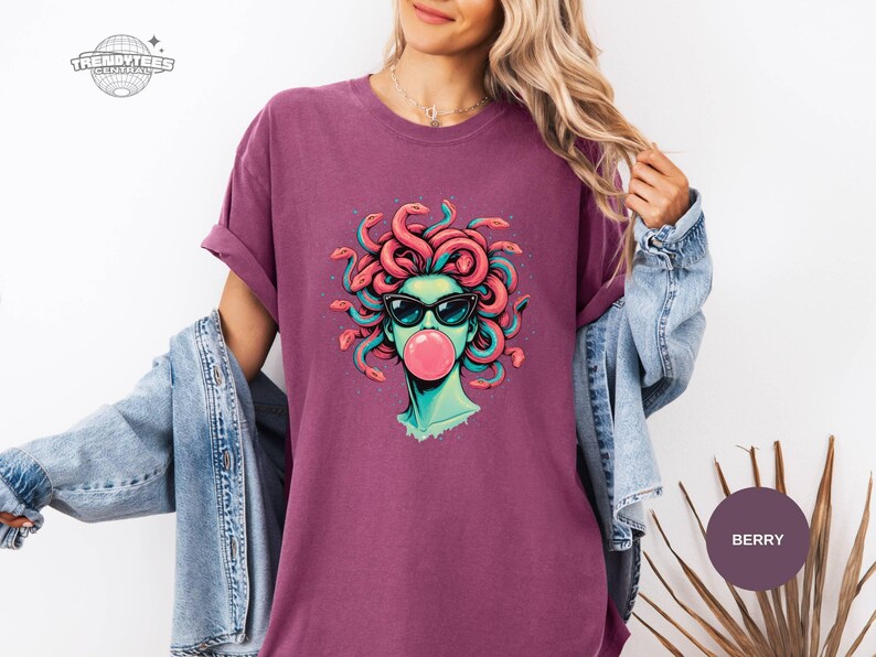 Berry purple Comfort Colors t-shirt showing a bright Medusa bubblegum graphic centered on the chest. The coral snakes and teal highlights stand out strongly on this deeper fashion color. Looks like an easy everyday statement tee for jeans and sneakers.