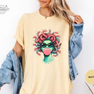 Butter pale yellow Comfort Colors shirt with the Medusa sunglasses and bubblegum graphic front and center. The soft yellow makes the teal face tones look extra fresh and summery. This color reads light, upbeat, and fashion-forward.