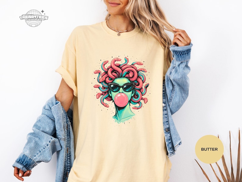 Butter pale yellow Comfort Colors shirt with the Medusa sunglasses and bubblegum graphic front and center. The soft yellow makes the teal face tones look extra fresh and summery. This color reads light, upbeat, and fashion-forward.