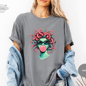 Grey Comfort Colors t-shirt featuring the Medusa sunglasses and bubblegum portrait. The mid-tone grey keeps the colors balanced, making the coral snakes and teal shading look clean and readable. This mockup fits a neutral, everyday style shopper.