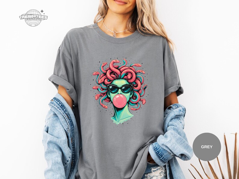 Grey Comfort Colors t-shirt featuring the Medusa sunglasses and bubblegum portrait. The mid-tone grey keeps the colors balanced, making the coral snakes and teal shading look clean and readable. This mockup fits a neutral, everyday style shopper.