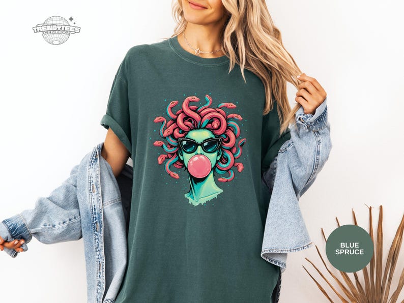 Blue Spruce deep green Comfort Colors t-shirt with the Medusa bubblegum portrait on the front. The dark green background makes the pink bubble and coral snakes pop with high contrast. Styled as a moody, modern mythology aesthetic.