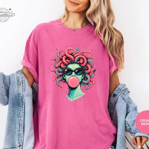 Crunchberry bright pink Comfort Colors tee with the Medusa bubblegum graphic centered. The bold shirt color turns the design into a playful statement while the black sunglasses keep it grounded. This one reads fun, girly, and confident.
