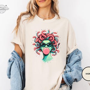 Ivory Comfort Colors tee with the Medusa bubblegum portrait centered on the chest. The creamy tone softens the overall look and gives the graphic a more boutique feel. Styled for a lighter neutral wardrobe and easy layering.