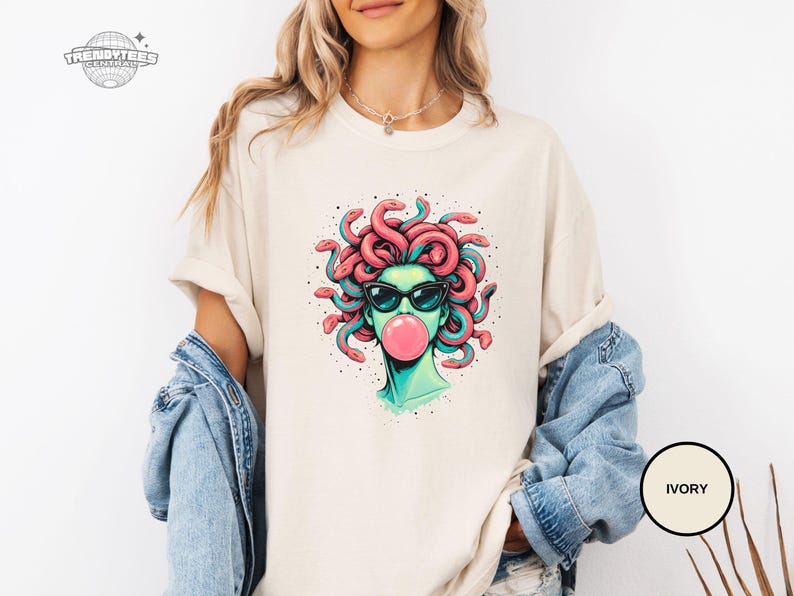 Ivory Comfort Colors tee with the Medusa bubblegum portrait centered on the chest. The creamy tone softens the overall look and gives the graphic a more boutique feel. Styled for a lighter neutral wardrobe and easy layering.