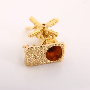 May include: Gold charm in the shape of a windmill. The charm is detailed and has a textured surface. The charm is a traditional Dutch design.