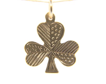 May include: A gold-colored shamrock pendant with detailed textures, suspended by a thin gold chain. The three-leaf clover design features various patterns, including lines and dots, adding visual interest to the jewelry. The pendant is against a white background.