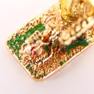 May include: Close-up of the bottom of a gold-colored charm with green and red enamel details. The charm is shaped like a carriage with a horse pulling it.