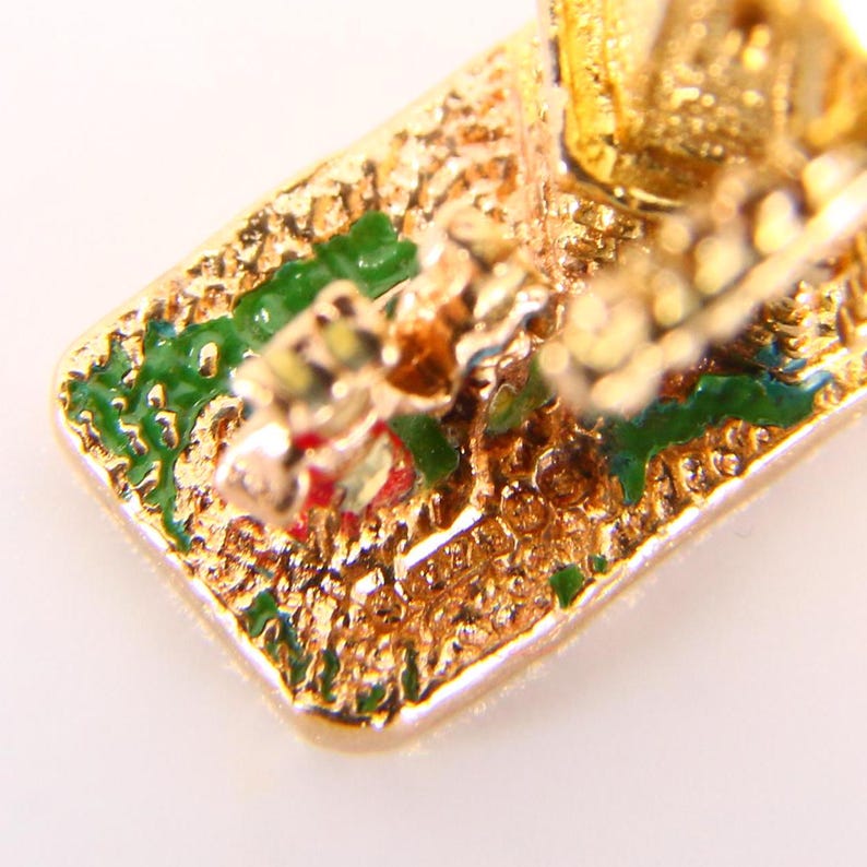 May include: Close-up of the bottom of a gold-colored charm with green and red enamel details. The charm is shaped like a carriage with a horse pulling it.