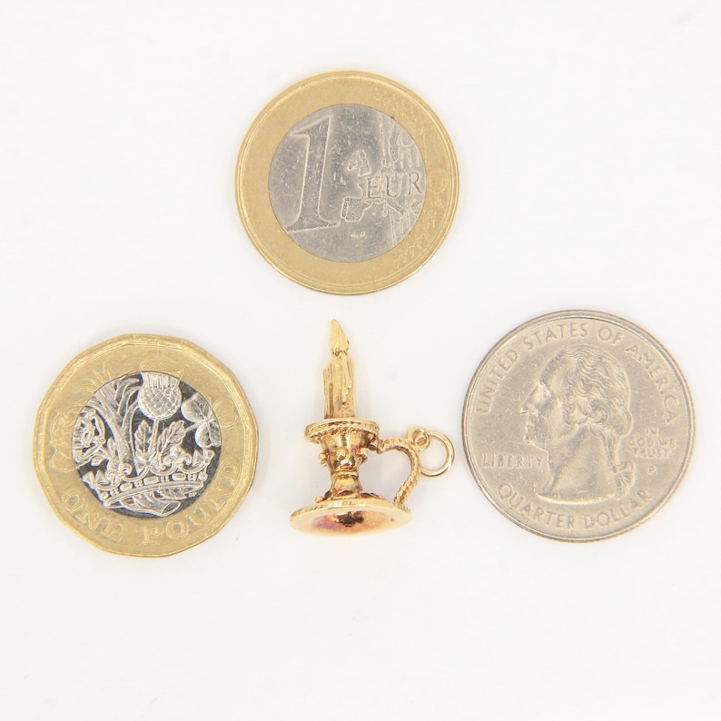 Puede incluir: Un charm de candelabro dorado con una vela encendida, un asa y una base redonda. El charm est&aacute; junto a una moneda de euro, una moneda de libra esterlina y un cuarto de d&oacute;lar estadounidense para comparar el tama&ntilde;o.